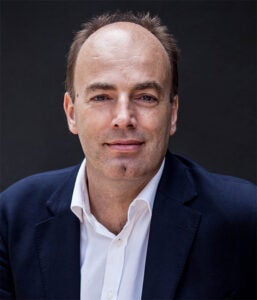 Professor Charlese Spence poses in front of a dark background, looking at the camera with a neutral expression.