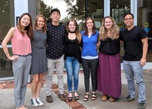 Seven people standing together and smiling in front of a building.