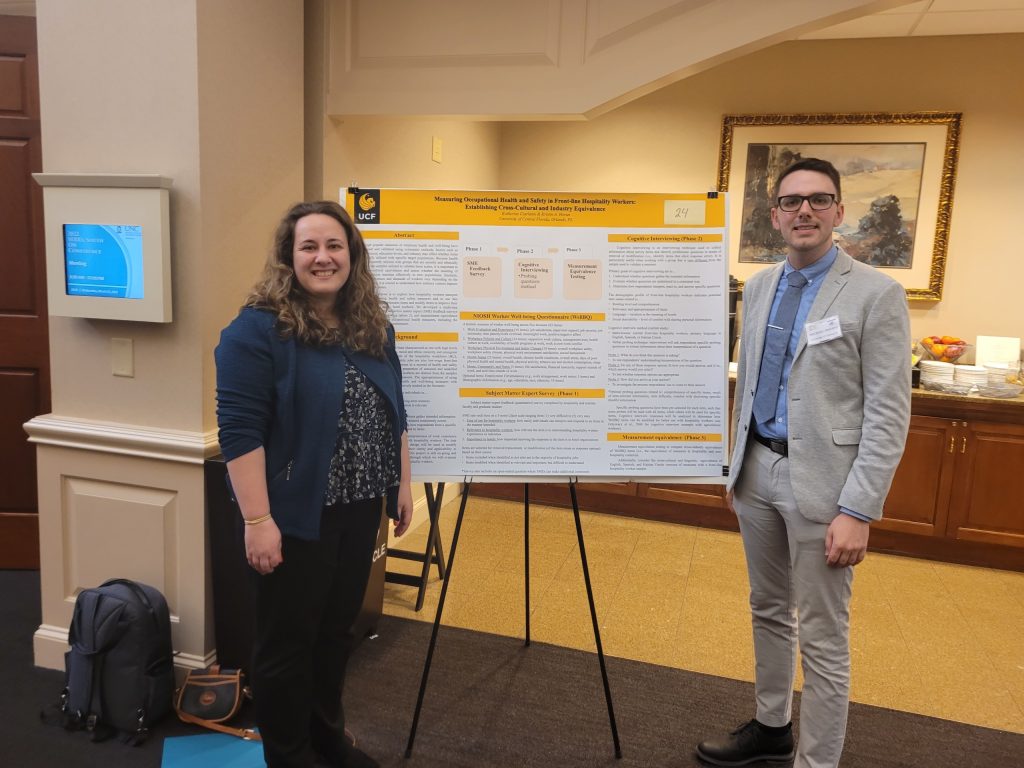 Two people stand beside a large research poster in a conference room.