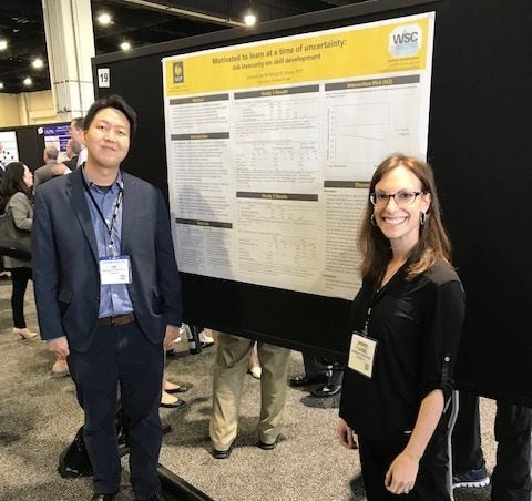 Two individuals stand in front of a scientific poster presentation at a conference.