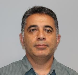 A middle-aged man with short gray hair and a trimmed beard wears a green checkered shirt, facing forward against a plain light background.