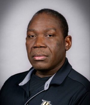 A man wearing a black UCF polo shirt poses in front of a plain gray background.