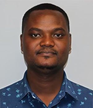 A man with short hair and a trimmed beard is wearing a blue shirt with a white pattern, posing against a plain light background.