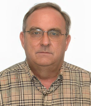 Middle-aged man with short hair, wearing glasses and a plaid button-up shirt, facing the camera against a plain white background.