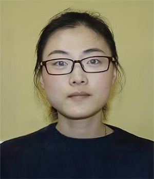A woman with glasses and dark hair pulled back is facing forward against a plain yellow background.