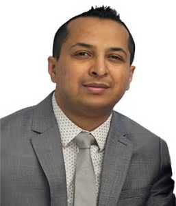 A man wearing a grey suit, light grey tie, and white shirt with small polka dots, posing against a white background.