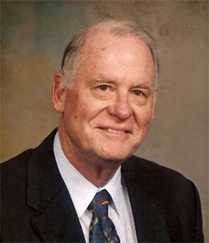 An older man in a suit and tie poses for a formal portrait against a neutral background.