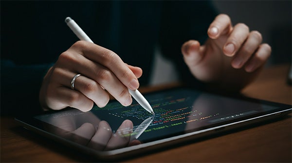 Person using a stylus to write code on a tablet screen displaying colorful text.