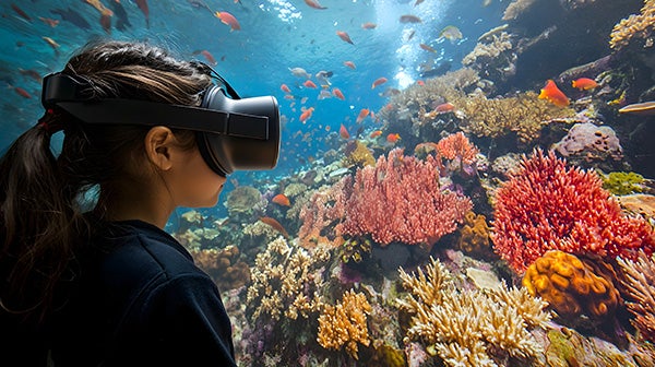 Person with virtual reality headset experiencing an underwater scene with colorful coral and fish.