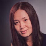 A woman with long, straight dark hair and a slight smile looks at the camera against a neutral background.
