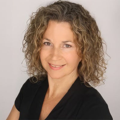 Woman with curly, shoulder-length hair wearing a black top, smiling slightly, posed against a plain light background.